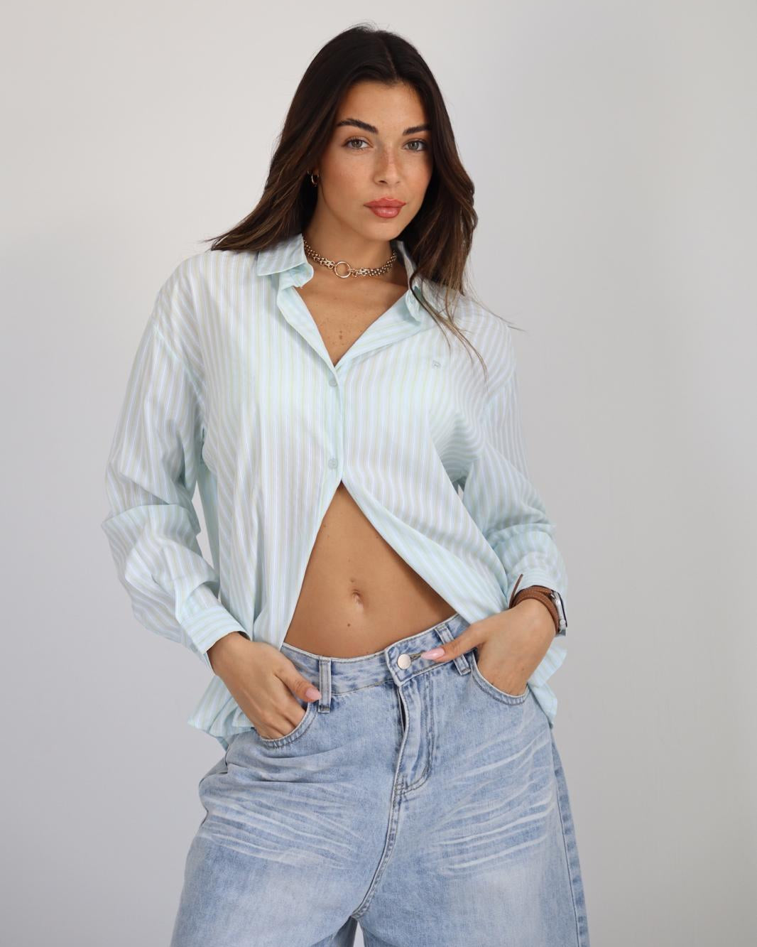 Woman wearing a light blue striped shirt and jeans against a plain background