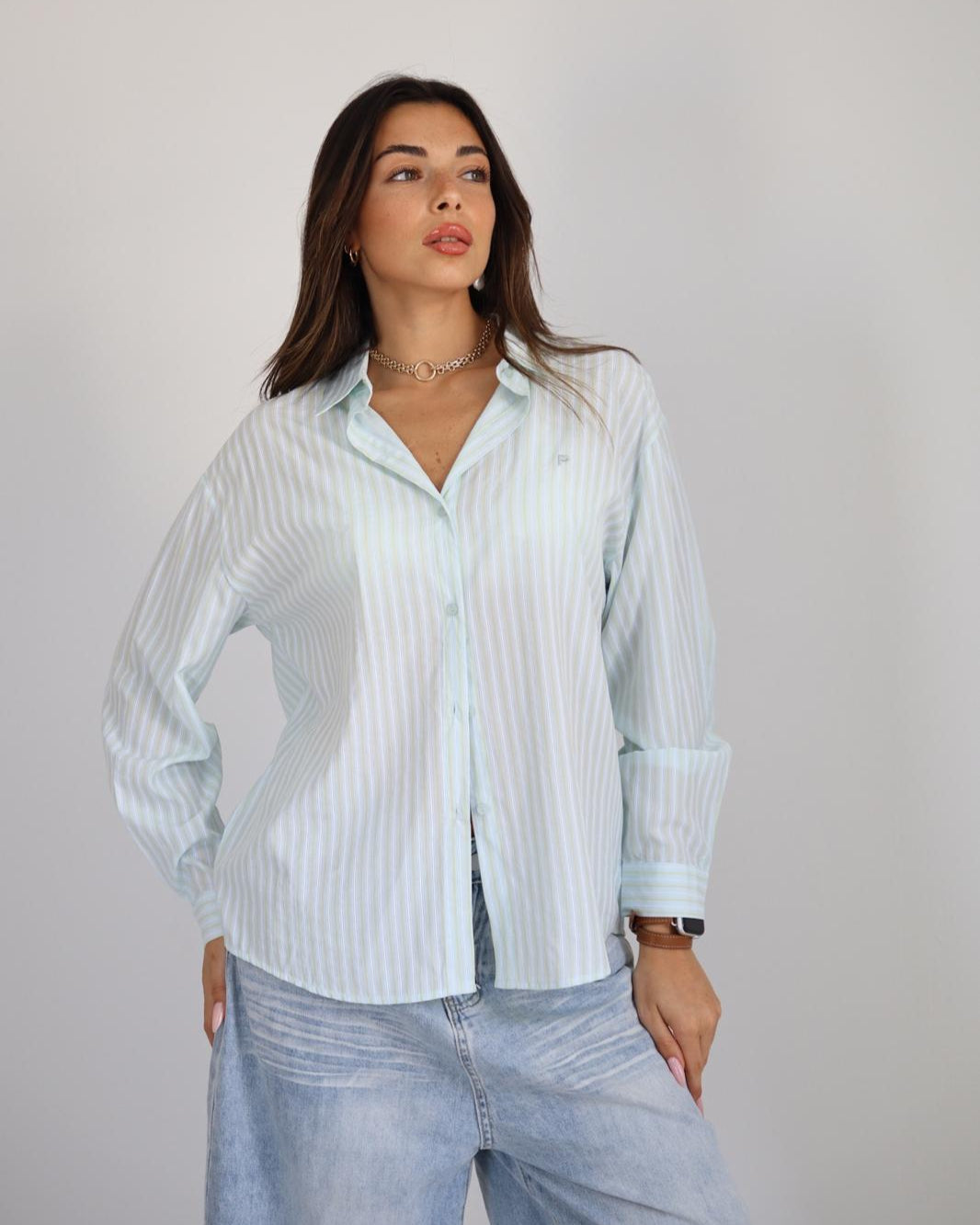 Woman wearing a light blue striped shirt and jeans against a plain background