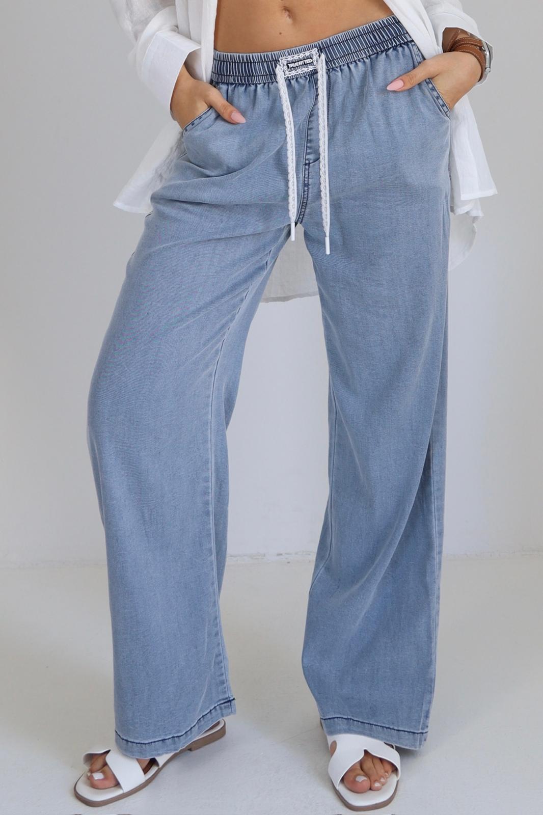 Person wearing light blue jeans with a drawstring waist on a plain background