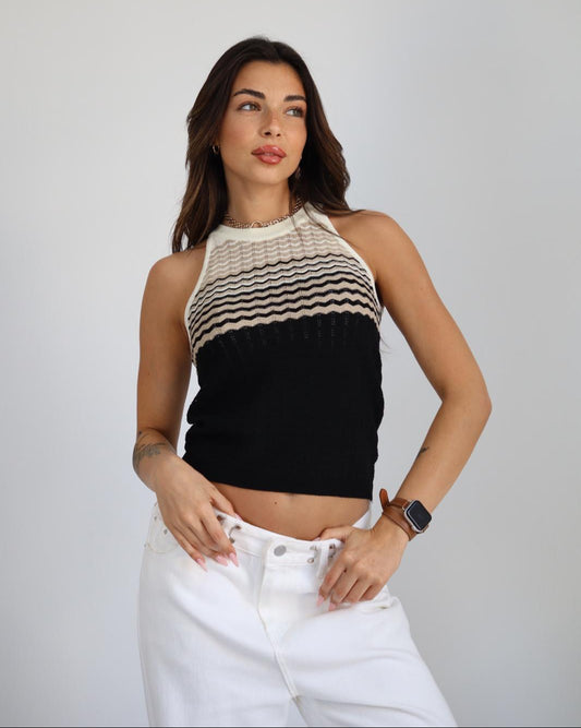 Woman wearing a black and white striped sleeveless top with white pants on a plain background