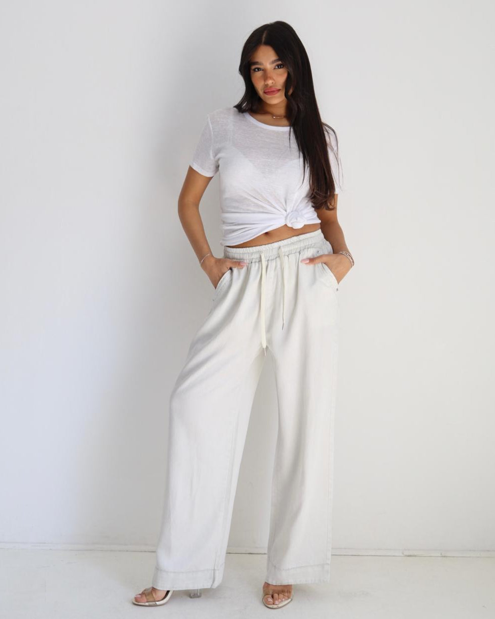 Woman wearing a white crop top and wide-leg pants against a plain background