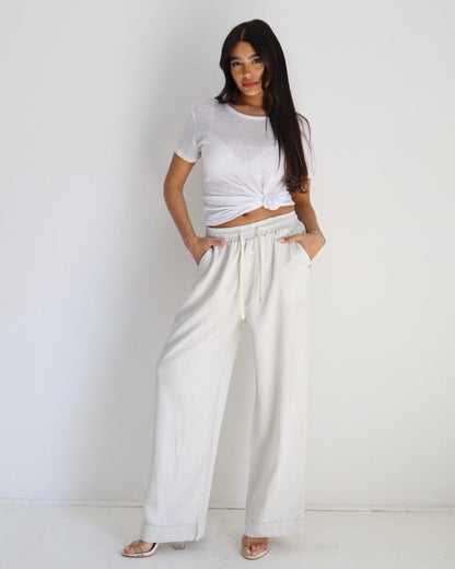 Woman wearing a white crop top and wide-leg pants against a plain background