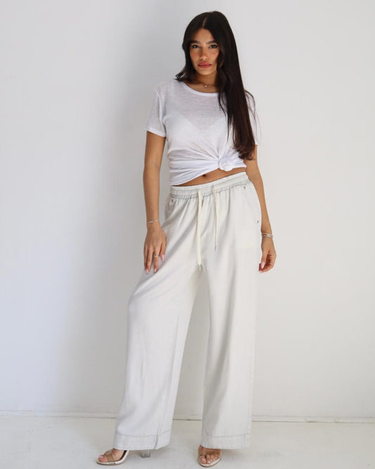 Woman wearing a white t-shirt and wide-leg pants against a plain background