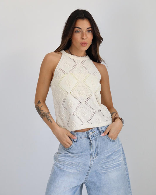 Woman wearing a sleeveless top with geometric patterns and high-waisted jeans against a plain background