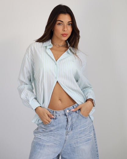 Woman wearing a light blue striped shirt and jeans against a plain background