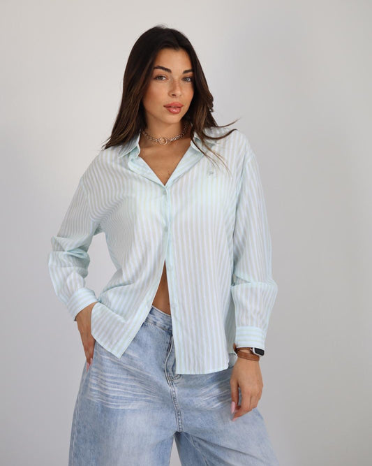 Woman wearing a light blue striped shirt and jeans against a plain background