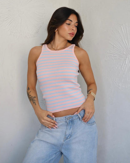 Woman wearing a pink and white striped tank top and light blue jeans against a textured white wall.