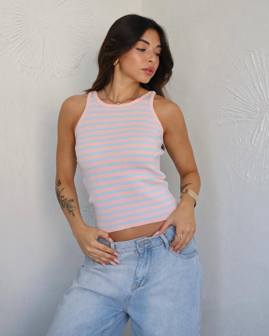 Woman wearing a pink and white striped tank top and light blue jeans against a textured white wall.