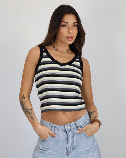 Woman wearing a black and white striped tank top and blue jeans against a plain background