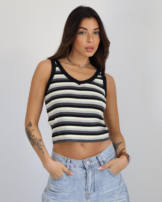 Woman wearing a black and white striped tank top and blue jeans against a plain background