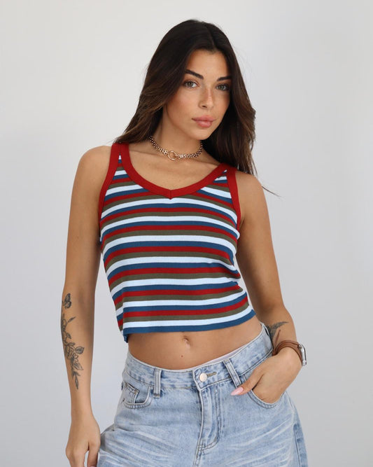 Woman wearing a red, white, and blue striped tank top with light blue jeans on a plain background