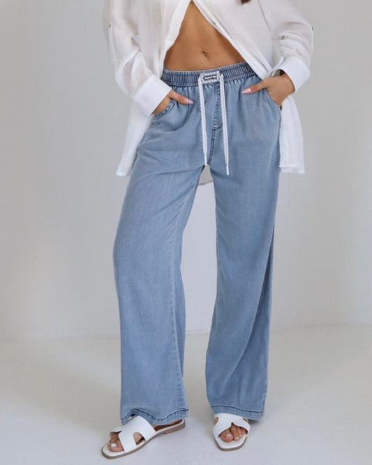 Woman wearing a white shirt and blue jeans against a plain background