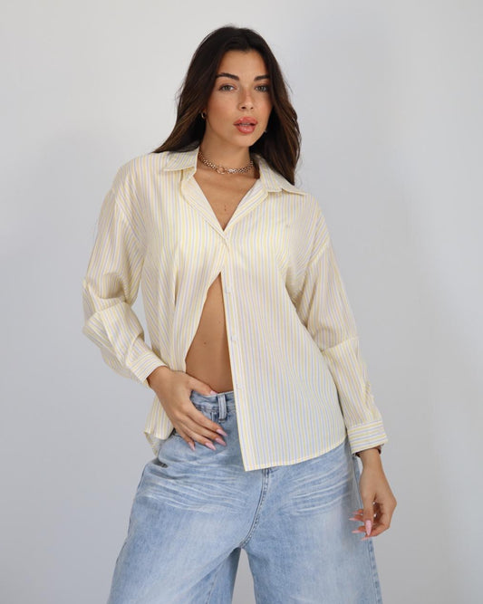 Woman wearing a white button-up shirt and light blue jeans against a plain background